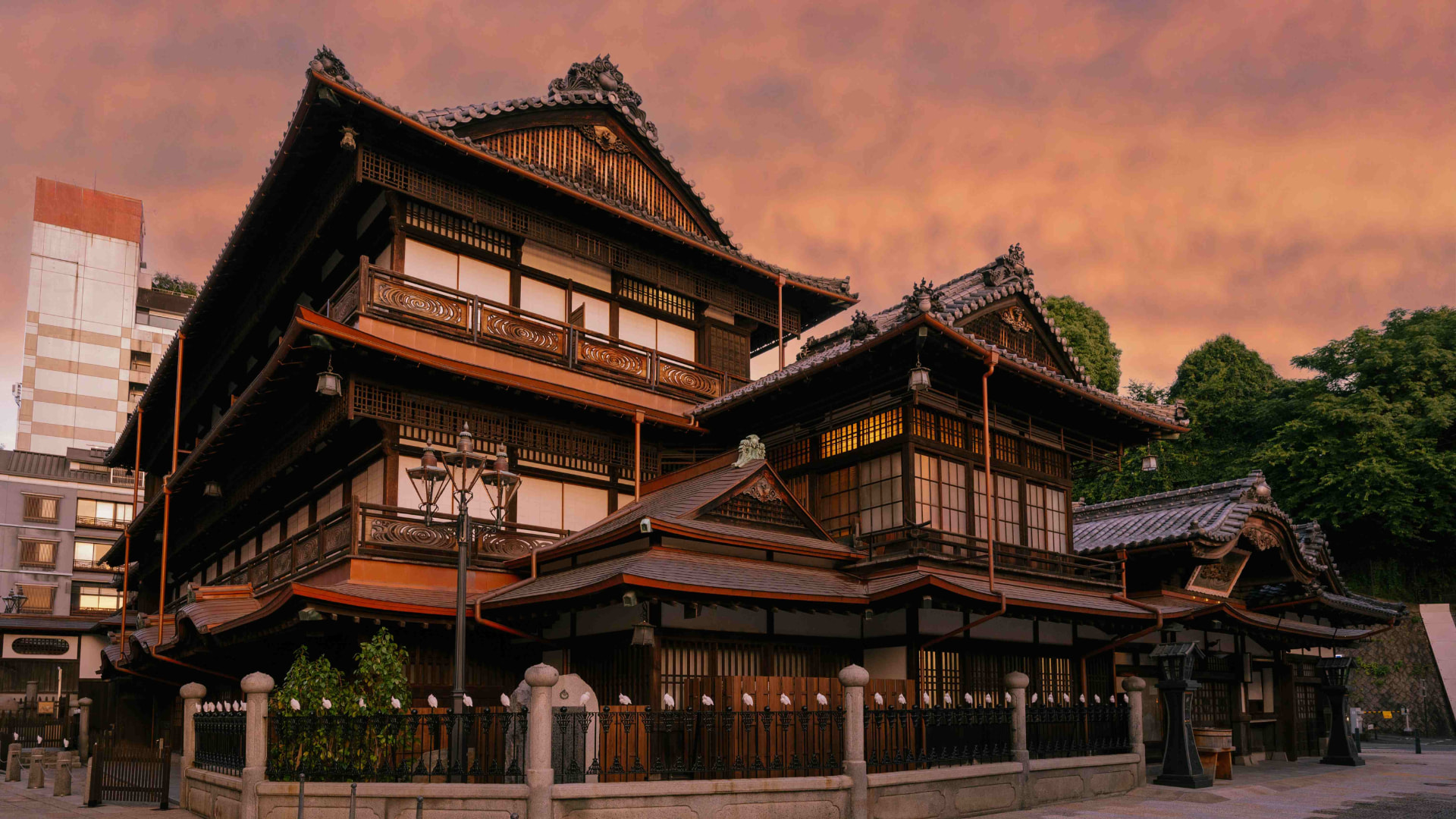 Dogo Onsen Honkan, the historic wooden bathhouse in Matsuyama, lit at dusk under a pink sky